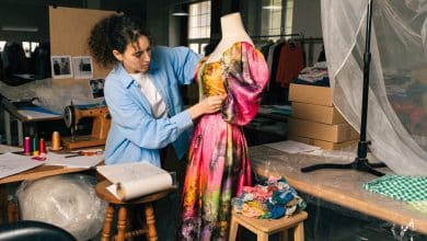 Estilista em uma oficina de moda criando um vestido colorido, com tecidos, moldes, acessórios e manequim ao redor