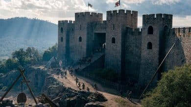 Fortaleza medieval de pedra cercada por muralhas, torres e máquinas de cerco durante uma batalha estratégica